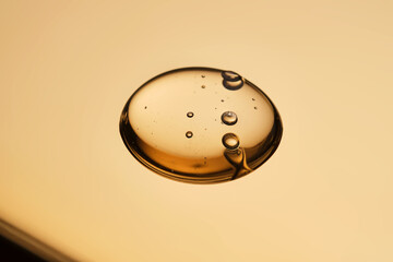 A beautiful drop of gel-like cosmetic serum with bubbles on a golden background.