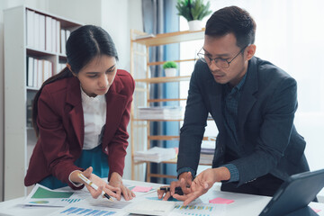 Focused Collaboration: Two business professionals, a man and a woman, intensely review documents and charts spread across a modern office desk, showcasing focused teamwork and strategic planning.