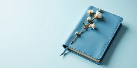 A serene blue leather journal adorned with delicate white blossoms rests on a light blue background, suggesting tranquility and peaceful contemplation
