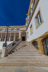 A grand stone staircase ascends towards an arched entrance of a white building with ornate details, framed against a deep blue sky.