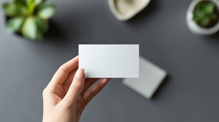 a hand holding a blank business card on a grey desk