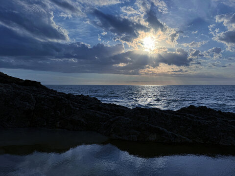 Evening sky clouds over sea and rocky coastline.