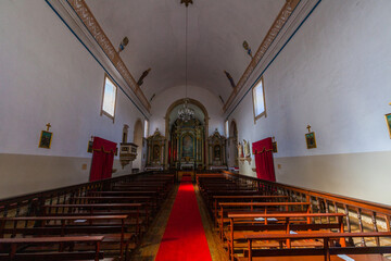 The interior of a simple church features a central aisle with wooden pews,