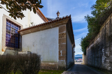 A small, white building with a terracotta-tiled roof and a stone trim sits adjacent to a larger...