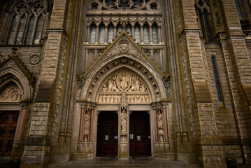 Obraz premium A detailed view of the ornate entrance to St. Colman's Cathedral in Cobh, Ireland, highlighting its elaborate stone carvings, statues, and Gothic architectural elements