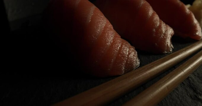 perfectly served uncooked meal, fresh nigiri sushi with raw pink salmon on a plate with gari and wooden chopsticks on black background