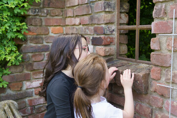 Two little girls looking into the old window of an old ruined house in summer. Concept of...