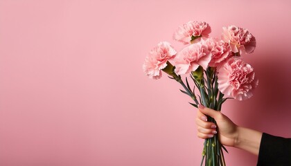 hand holding bouquet of carnations on pink background