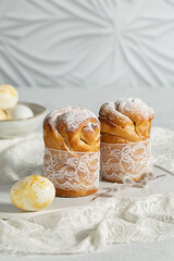 Two easter cakes sprinkled with powdered sugar, painted eggs and pussy willow twigs on white background. Easter treat, holiday symbol 