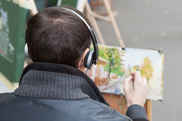 Rear view of a street artist painting a cityscape while sitting at an easel.