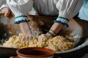 A person kneads dough with skilled hands in a rustic kitchen setting, wearing a traditional embroidered blouse, showcasing cultural heritage through culinary practice.