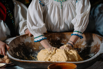A person wearing traditional clothing kneads dough in a large bowl, highlighting cultural culinary traditions and hands-on baking techniques.