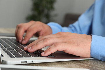 Businessman using laptop at wooden table, closeup. Modern technology