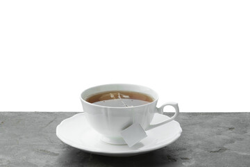 Tea bag in cup with hot drink on gray textured table against white background