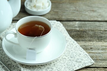Tea bag in cup with hot drink on wooden table, closeup. Space for text