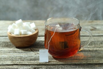 Tea bag in glass cup with hot drink and sugar cubes on wooden table