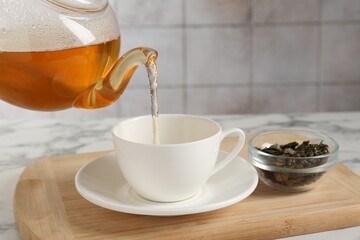 Pouring refreshing green tea from teapot into cup at white marble table, closeup
