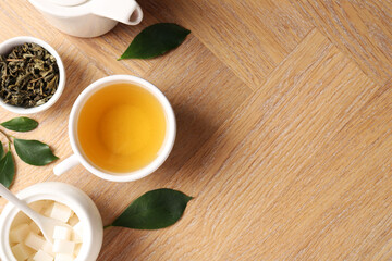 Refreshing green tea in cup, teapot, sugar bowl and leaves on wooden table, flat lay. Space for text