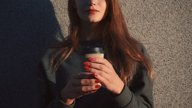 Unrecognizable Young Woman Generation Z in casual wear holding a disposable paper coffee cup looking happy, standing on a wall background in gold sunset light  4K UHD B-Roll footage
