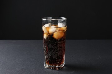 Refreshing cola with ice cubes in glass on black table, closeup