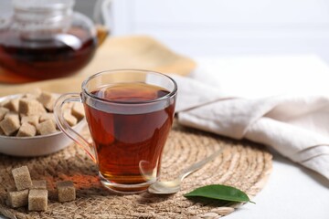 Aromatic black tea in cup and brown sugar cubes on white table, closeup. Space for text