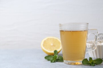Aromatic mint tea in glass cup, fresh leaves and lemon on light gray table against white background, space for text