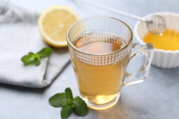 Aromatic mint tea in glass cup, fresh leaves, honey and lemon on light gray table, closeup