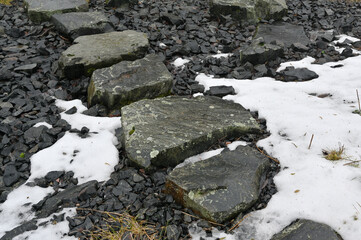 A rustic stone path winds through a rugged landscape, partially covered by melting snow
