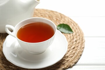 Aromatic black tea in cup and teapot on white wooden table, closeup