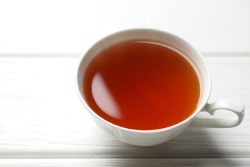Aromatic black tea in cup on white wooden table, closeup