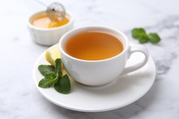 Aromatic mint tea in cup, fresh leaves and lemon on light marble table, closeup