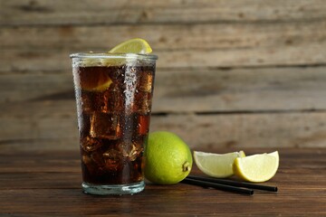 Refreshing iced cola with lemon slices and lime on wooden table. Space for text