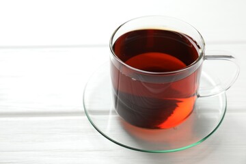 Aromatic black tea in cup on white wooden table, closeup. Space for text