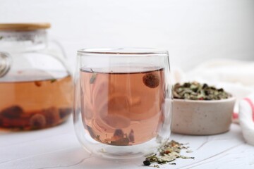 Delicious herbal tea and dry leaves on white table, closeup