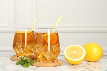 Refreshing iced tea with slices of lemon, mint and drinking straws on white marble table