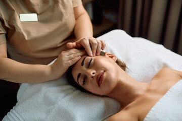 Smiling woman enjoying in head massage during treatment at health spa.
