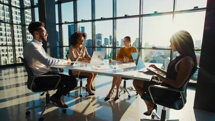 Three colleagues engage in a casual meeting in a sunlit office, fostering collaboration and creativity against a vibrant backdrop of city life