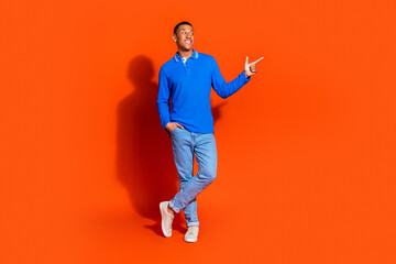 Young stylish man in blue polo posing against a vibrant orange background
