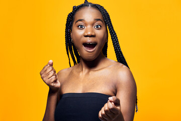Young Black woman expressing joy and surprise against a vibrant yellow background, showcasing her excitement with open hands and a big smile