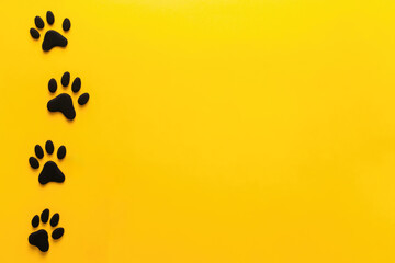 Minimalist design with black cat paw prints on vibrant yellow background with copy space. For pet-related projects, creative designs, advertisements that convey playfulness, energy, and feline charm
