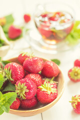 Fresh strawberries and mint leaves filling a wooden bowl with strawberry tea in the background