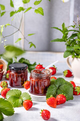 Homemade strawberry jam in glass jars with fresh strawberries and leaves