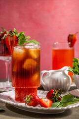Refreshing strawberry iced tea with fresh mint and ice on pink background