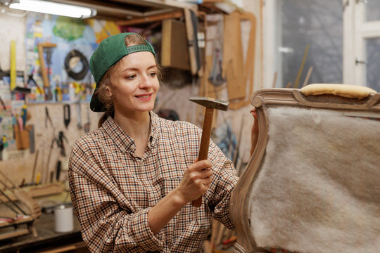 woman restores old wooden chair, works with hammer, concept of repair and restoration of old furniture. Copy space