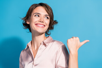 Young woman with a stylish bob haircut in a pink satin blouse, smiling confidently against a blue background, exuding charm and happiness