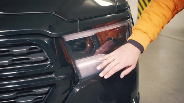 Closeup video, The man touches his hand to left car headlight side span of the camera. 