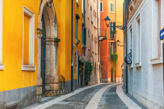 Medieval narrow street with colorful building facades and cobblestone pavement in Verona old town, Veneto, Italy at sunrise. Italian street with nobody. Travel destination in Europe