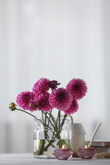 Beautiful pink flowers in vase and burning candles on wooden table at home. Space for text