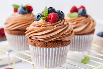 Tasty cupcakes with chocolate cream and berries on white table, closeup