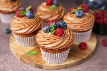 Tasty cupcakes with chocolate cream and berries on brown table, closeup